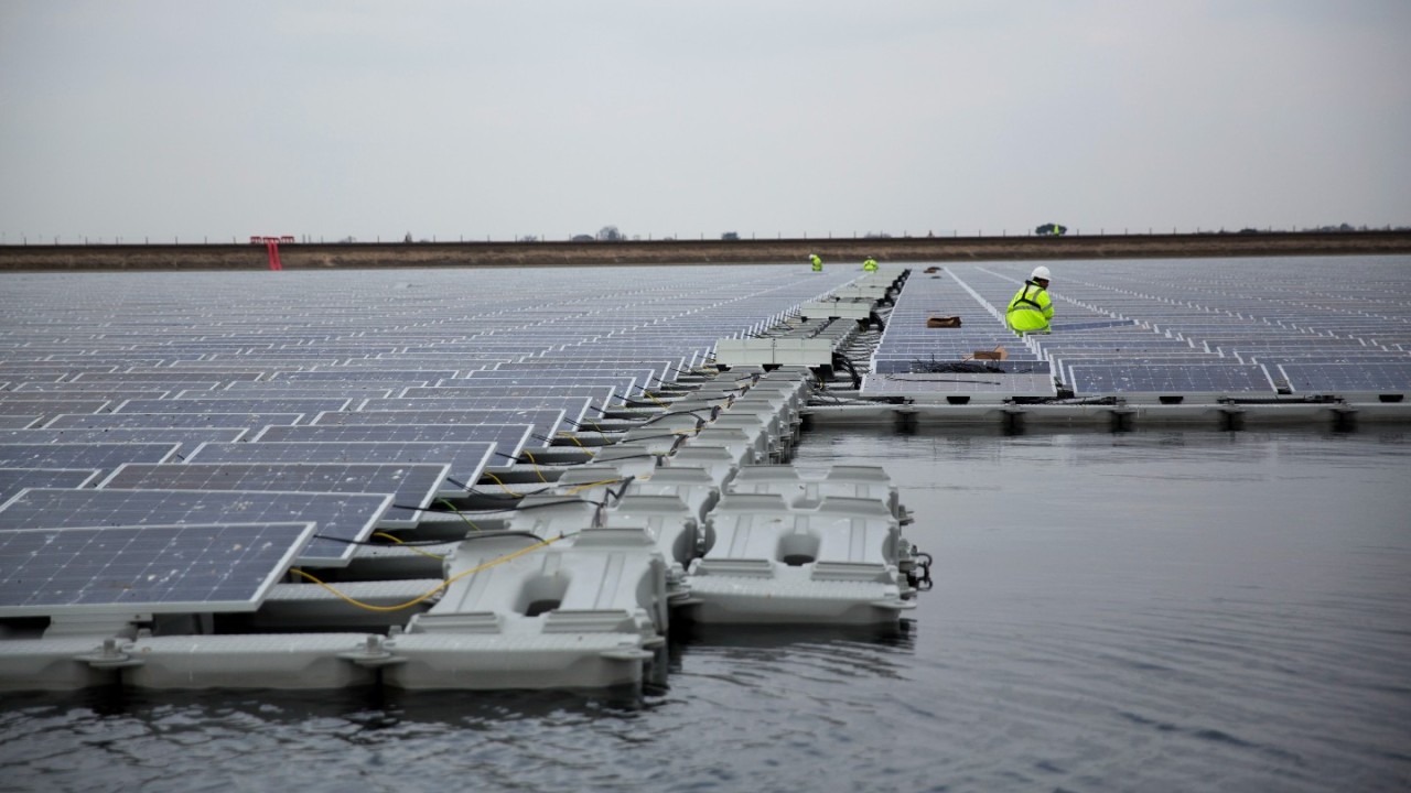 Ao fundo da imagem uma lagoa e uma usina solar flutuante, feita de placas solares, sobre a água